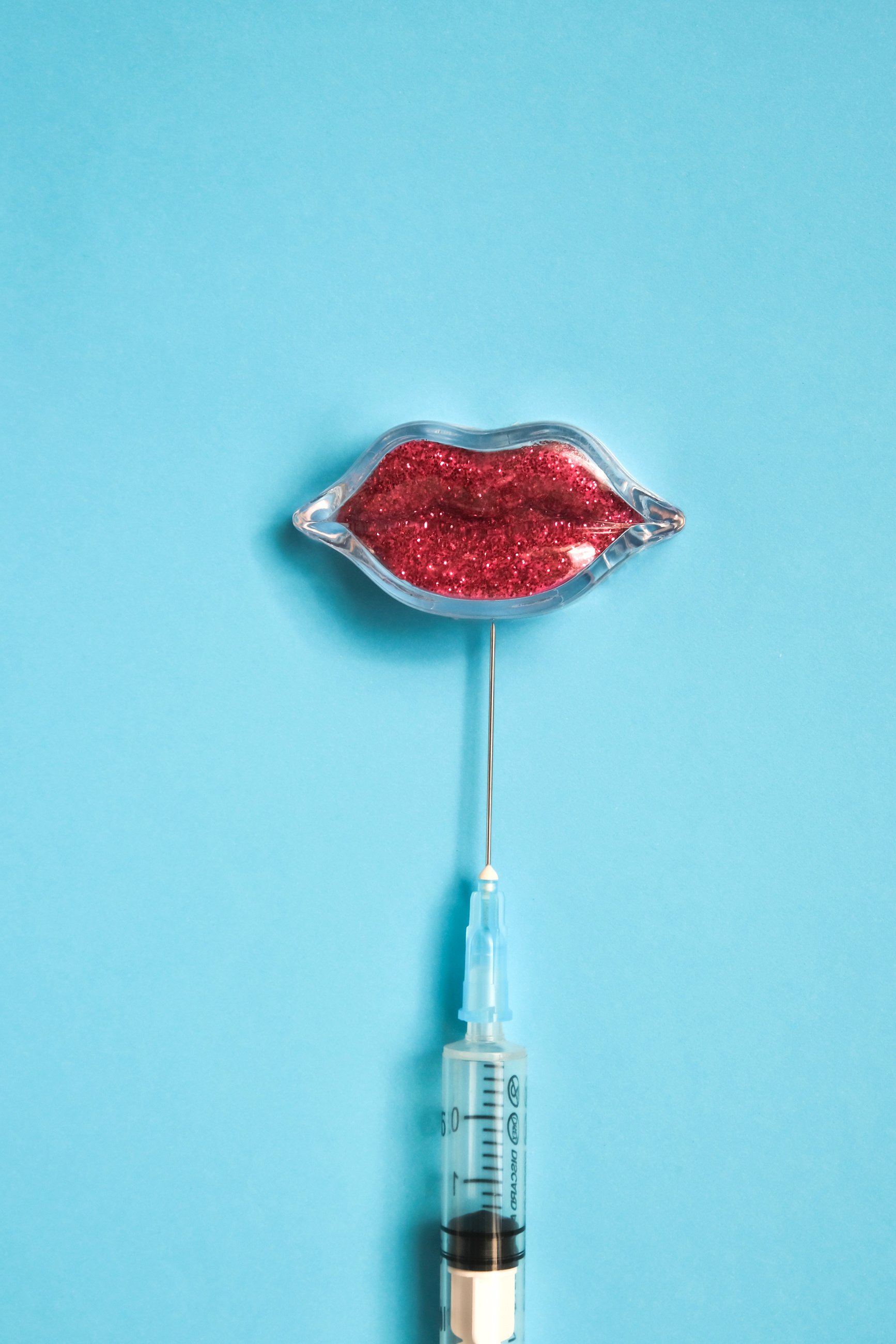 Lips and injection syringe with hyaluronic acid on a blue ba